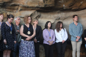 eight people standing against sandstone rock in cave, listening to someone off camera speaking