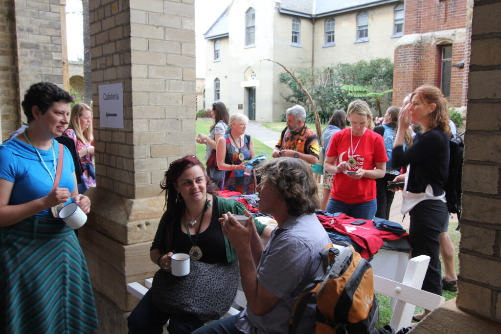 people seated and standing outdoors chatting with cups of tea