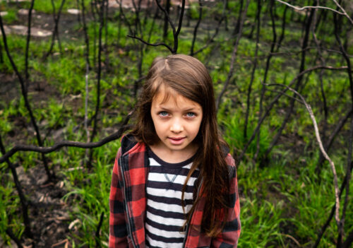 young girl in fire ravaged landscape that is regenerating, looking at camera